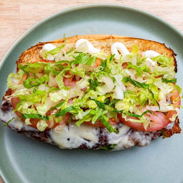 Toasted bagel sandwich with melted cheese, tomatoes, shredded lettuce, and mayonnaise on a blue plate.
