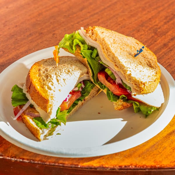 A turkey and cheese sandwich with lettuce, tomato, and onion on whole wheat bread, cut in half.