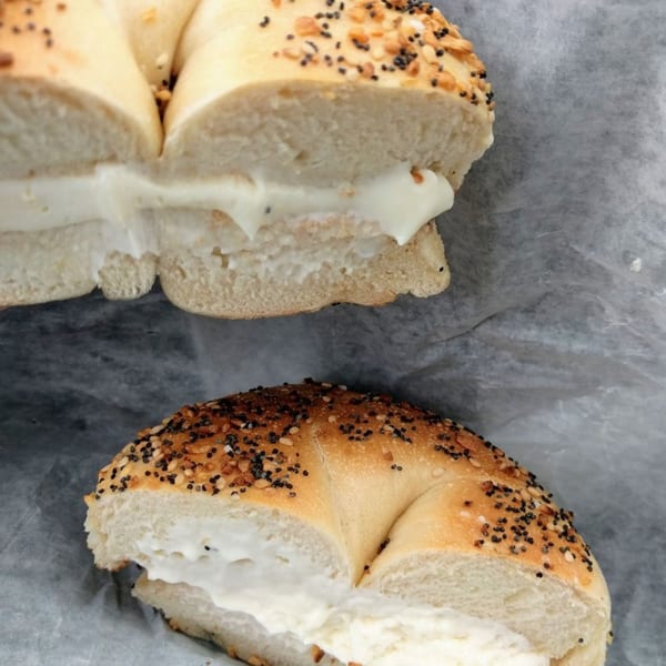 Two halves of an everything bagel from Bagels N' Crumbs, generously filled with cream cheese.