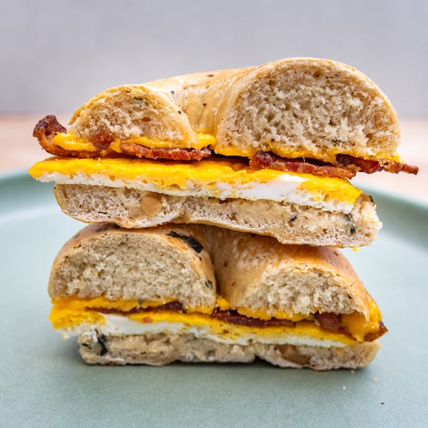Two halves of a bagel sandwich stacked, filled with egg, cheese, and bacon on a green plate.