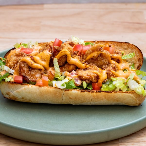 A shrimp po'boy sandwich on a green plate, filled with fried shrimp, lettuce, tomatoes, and sauce.