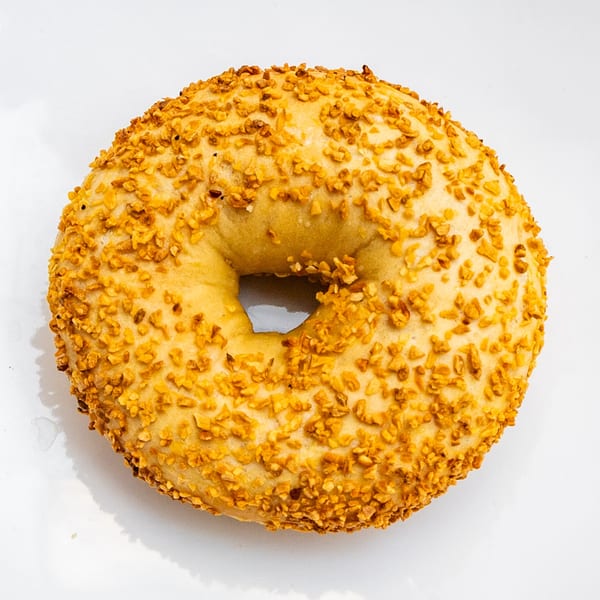 A golden-brown bagel from Bagels N' Crumbs, generously topped with crunchy garlic pieces on a white surface.